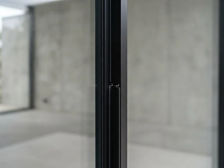 Close-up of a minimal-frame sliding door interlock showing the slim aluminium profile between glass panels
