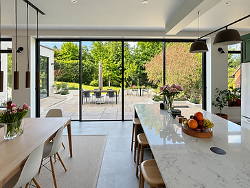 Bright open-plan kitchen and dining area opening onto a garden patio through full-width black-framed sliding glass doors