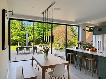 Restored period interior with a large seamless glass wall of minimal-frame sliding doors opening onto a garden, neutral gallery-like backdrop