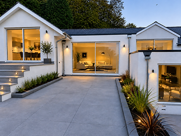 Modern single-storey courtyard extension at dusk with floor-to-ceiling glass sliding doors opening onto a stone patio with warm downlighting