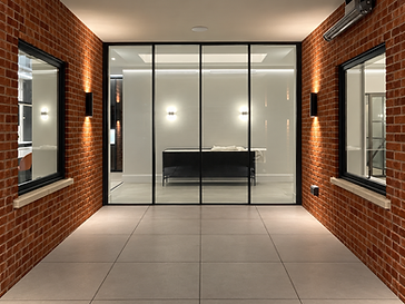 Symmetrical interior corridor with red brick walls and a floor-to-ceiling four-pane glass partition wall with thin black frames