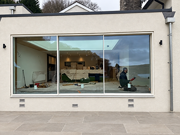 Off-white rendered extension with three large cream-framed sliding glass panels over a light stone patio, captured during fit-out