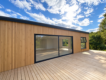 Contemporary oak-clad garden room with a large black-framed sliding glass door partially open onto a matching timber deck in bright sunlight
