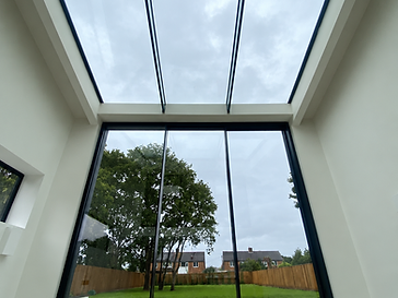 Interior looking out through floor-to-ceiling minimal-frame sliding glass doors with an integrated glass skylight above, toward a stepped garden