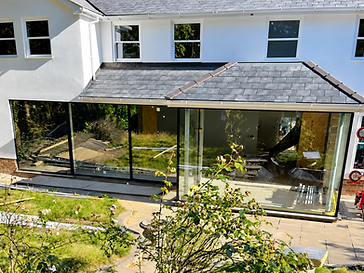 Single-storey rear extension with a pitched slate roof and wide multi-panel floor-to-ceiling sliding glass doors, viewed from the garden during installation