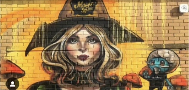 Portrait mural of a woman in a witch hat on a yellow brick wall