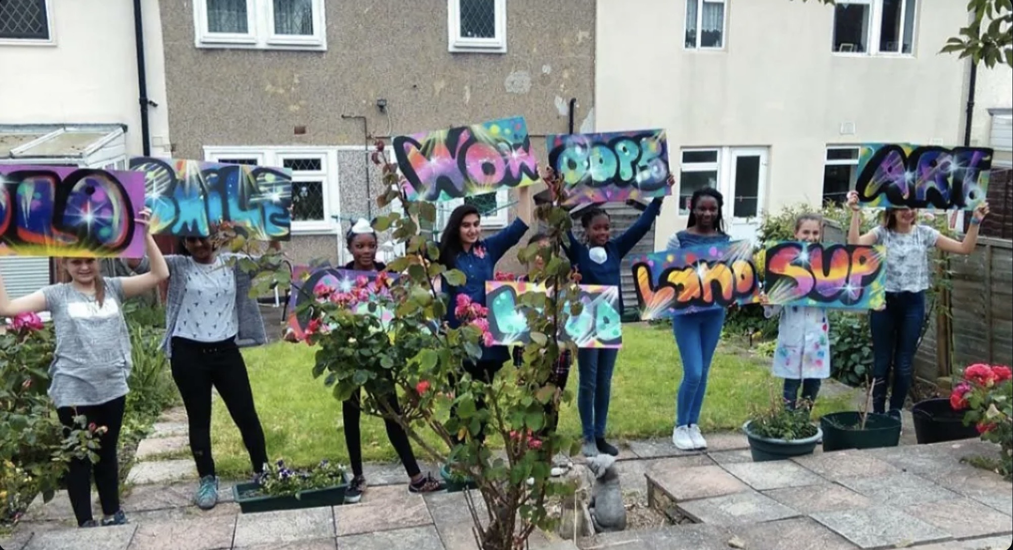 Young people holding up colourful graffiti boards in a garden