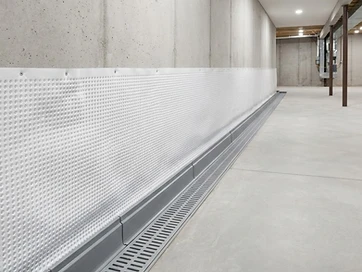 A dry, professionally waterproofed basement foundation wall with a moisture barrier, perimeter drainage channel, and sealed concrete