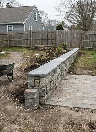 Residential fieldstone wall construction beside a paver patio