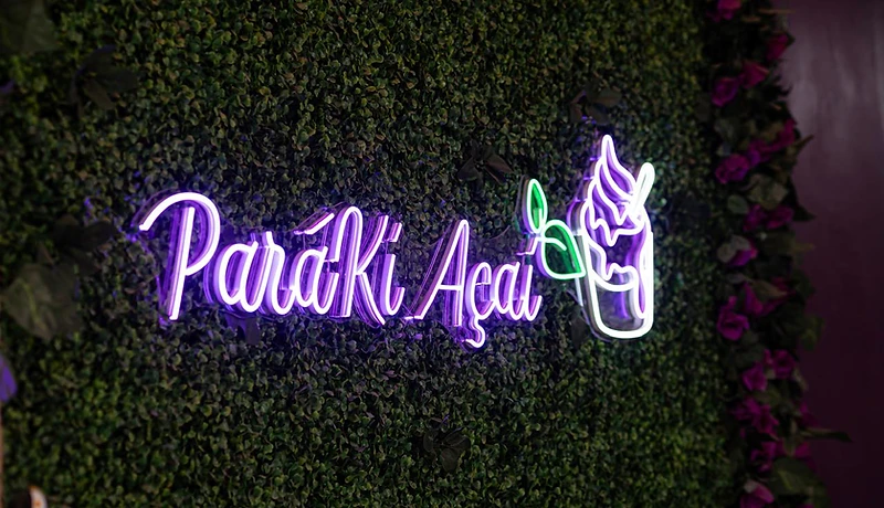 Letreiro neon 'Paráki Açaí' na parede verde da loja