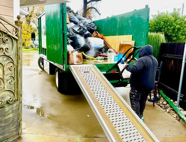 Dump Day crew loading a green dump truck on a residential driveway