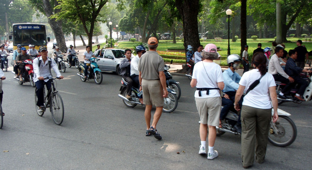 Tourists crossing a busy street in Vietnam surrounded by motorbikes and bicycles