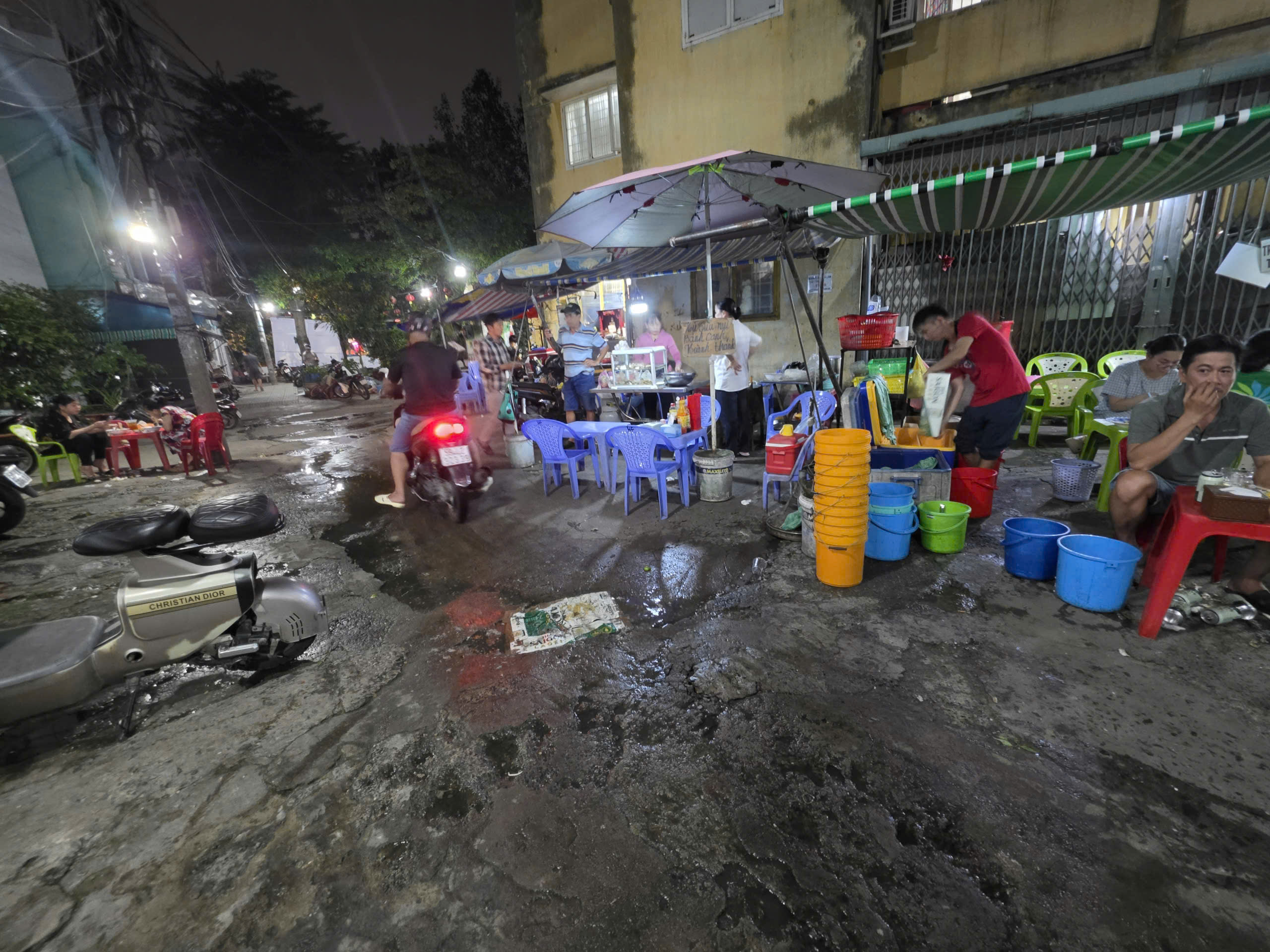 Vietnamese nighttime street seafood scene with plastic chairs, umbrellas, scooters, and a street-side food stall