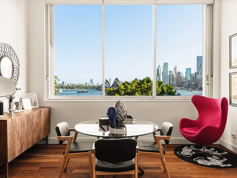 Styled interior with a red sculptural chair and windows overlooking a marina