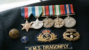 Realistic illustration of the military medals and badges awarded to Betty Withers, shown against a light United Kingdom flag background. AI-generated illustration, not an authentic photograph.