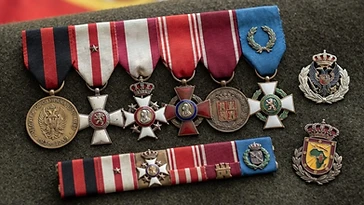 Realistic illustration of the military medals and badges awarded to Francisco Franco, including Campaign Medal of the Civil War, Long Military Service Cross, Royal and Military Order of Saint Hermenegild, Cross of Military Merit with Red Decoration, Military Medal, Laureate Cross of Saint Ferdinand, shown against a light Spain flag background. AI-generated illustration, not an authentic photograph.