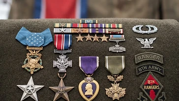 Realistic illustration of the military medals and badges awarded to Ralph Puckett Jr., including Medal of Honor, Distinguished Service Cross, shown against a light North Korea flag background. AI-generated illustration, not an authentic photograph.