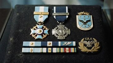 Realistic illustration of the military medals and badges awarded to Ernesto Rubén, including Order of Aeronautical Merit, Medal of Valour in Combat, shown against a light Argentina flag background. AI-generated illustration, not an authentic photograph.