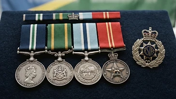 Realistic illustration of the military medals and badges awarded to Frank Short, including Royal Solomon Islands Police Long Service and Good Conduct Medal, Solomon Islands Prison Service Meritorious Medal, Royal Solomon Islands Police International Law Enforcement Cooperation Medal, Solomon Islands Police Bravery Medal, shown against a light Solomon Islands flag background. AI-generated illustration, not an authentic photograph.