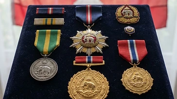 Realistic illustration of the military medals and badges awarded to Souvanna Phouma, including Order of Civic Merit of Laos, National Gold Medal, Medal of Government Gratitude, shown against a light Laos flag background. AI-generated illustration, not an authentic photograph.