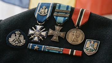 Realistic illustration of the military medals and badges awarded to Gheorghe Avramescu, including Order of Faithful Service, Commemorative Cross of the 1916–1918 War, Crusade Against Communism Medal, shown against a light Romania flag background. AI-generated illustration, not an authentic photograph.