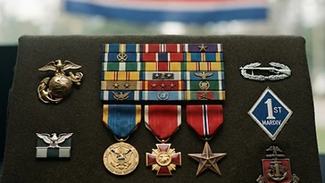 Realistic illustration of the military medals and badges awarded to Chesty Puller, including Navy Distinguished Service Medal, Legion of Merit, Bronze Star, shown against a light North Korea flag background. AI-generated illustration, not an authentic photograph.