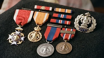 Realistic illustration of the military medals and badges awarded to Vang Pao, including Order of the Million Elephants and the White Parasol, Order of the Crown of Laos, Order of Freedom, Combat Veterans Medal, shown against a light Laos flag background. AI-generated illustration, not an authentic photograph.