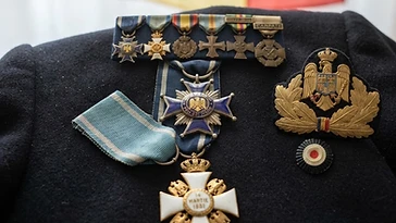 Realistic illustration of the military medals and badges awarded to Alexandru Averescu, including Order of the Crown of Romania, Order of the Star of Romania, shown against a light Romania flag background. AI-generated illustration, not an authentic photograph.