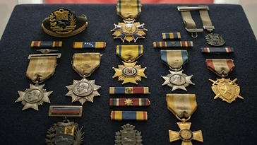Realistic illustration of the military medals and badges awarded to Eleazar Lopez Contreras, including Cross of the Venezuelan Army, Military Order of General Rafael Urdaneta, Military Order of General Jose Antonio Paez, Military Order of National Defense, Order of Army Merit, Star of Carabobo Decoration, shown against a light Venezuela flag background. AI-generated illustration, not an authentic photograph.