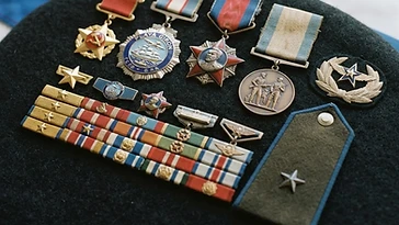 Realistic illustration of the military medals and badges awarded to Arnaldo Tamayo Méndez, including Gold Star of a Hero of the Republic of Cuba, Order of Playa Girón, Order of Máximo Gómez, Medal of Combat Fraternity, shown against a light Cuba flag background. AI-generated illustration, not an authentic photograph.