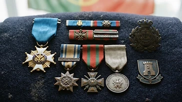 Realistic illustration of the military medals and badges awarded to Aníbal Milhais, including Military Order of the Tower and of the Sword, of Valor, Loyalty and Merit, shown against a light Portugal flag background. AI-generated illustration, not an authentic photograph.