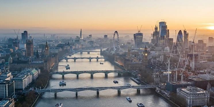 Aerial view over a UK city river skyline with bridges, towers and construction cranes at sunrise