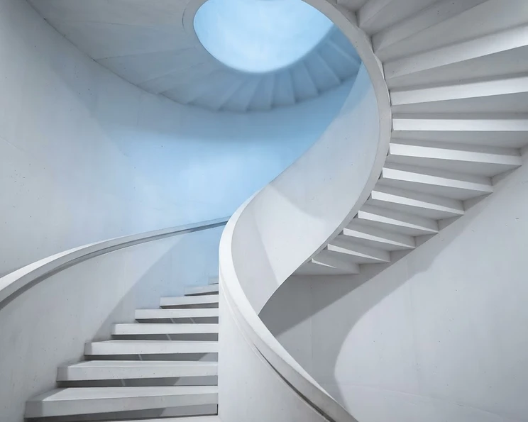 Minimal white concrete spiral staircase in soft blue light representing precision