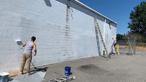 Commercial Wall Repaint — Our crew rolling fresh white coating across a long commercial block wall — full drop-cloth and ladder setup on site.
