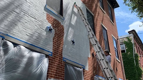 Brick Row House — In Progress — Fresh white sections going up on a red-brick row house, with windows masked and drop cloths protecting every opening.
