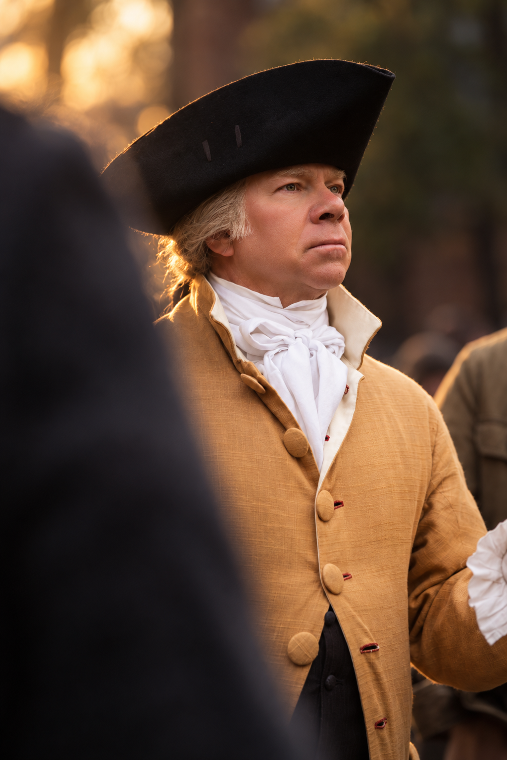 Editorial portrait of a man in a tricorn hat and colonial cravat, photographed in profile in warm outdoor light