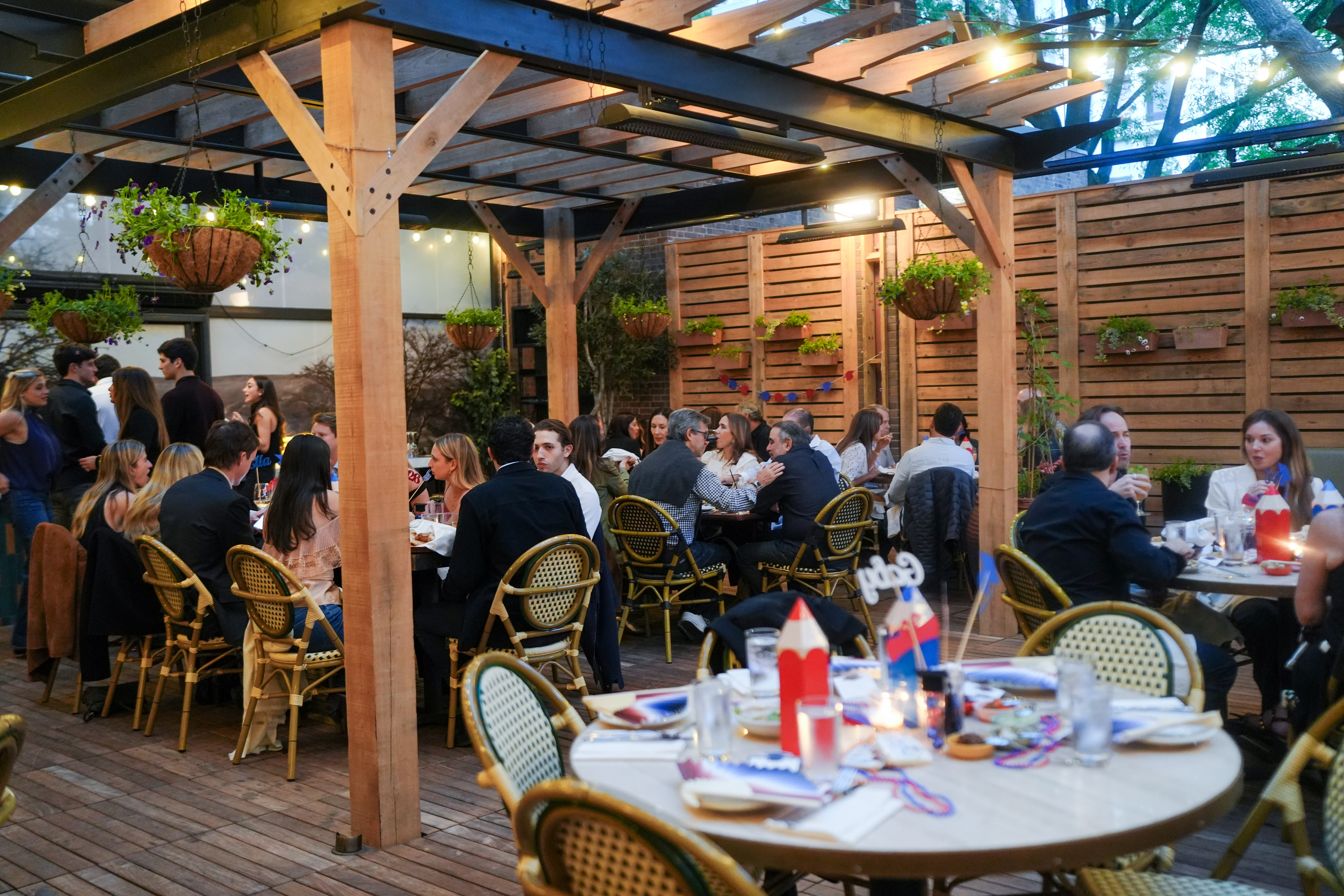 Guests gathered at an outdoor evening dinner under a pergola strung with warm string lights