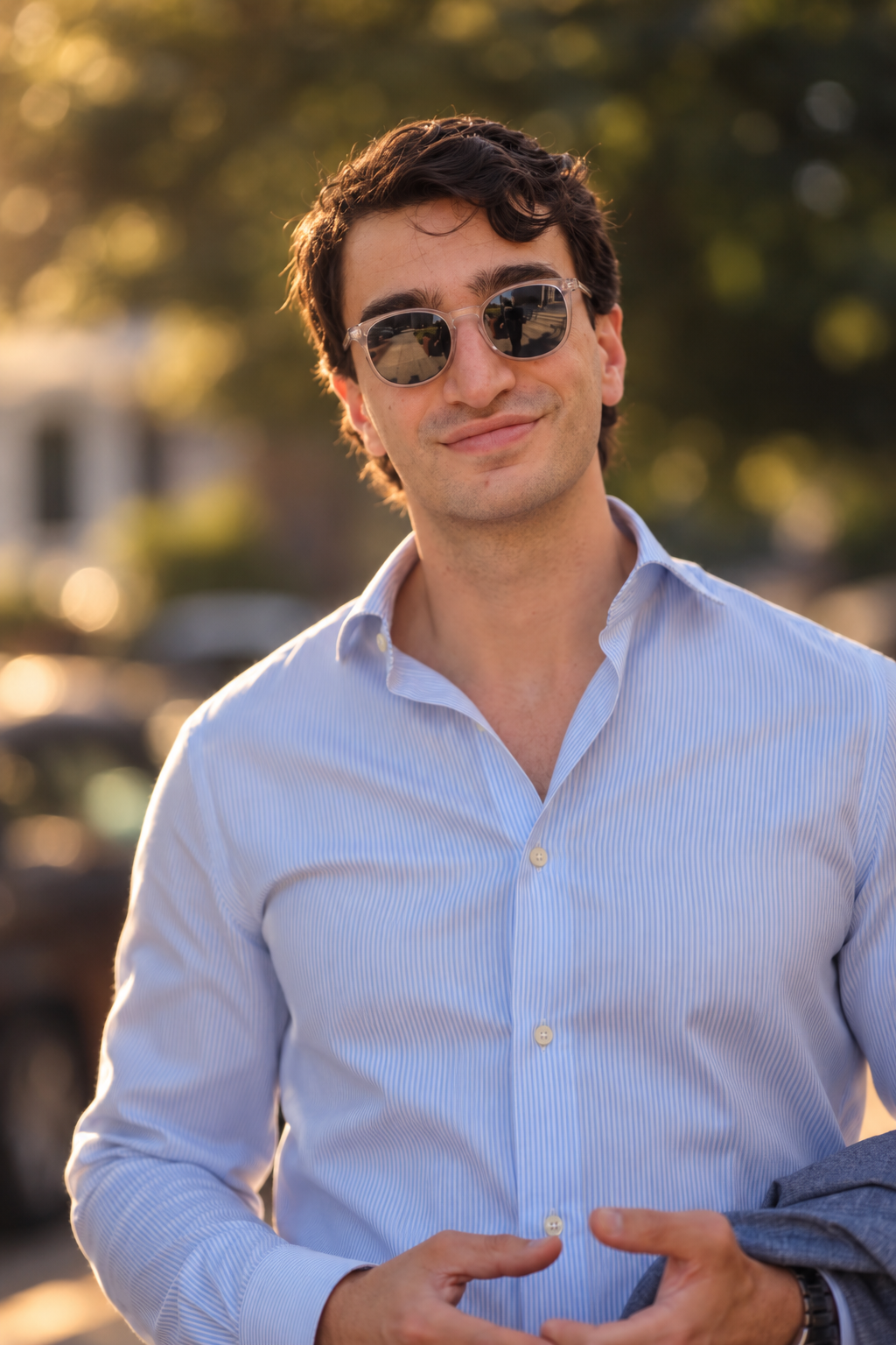Portrait of a man in sunglasses and an open-collar blue shirt in golden-hour light outdoors