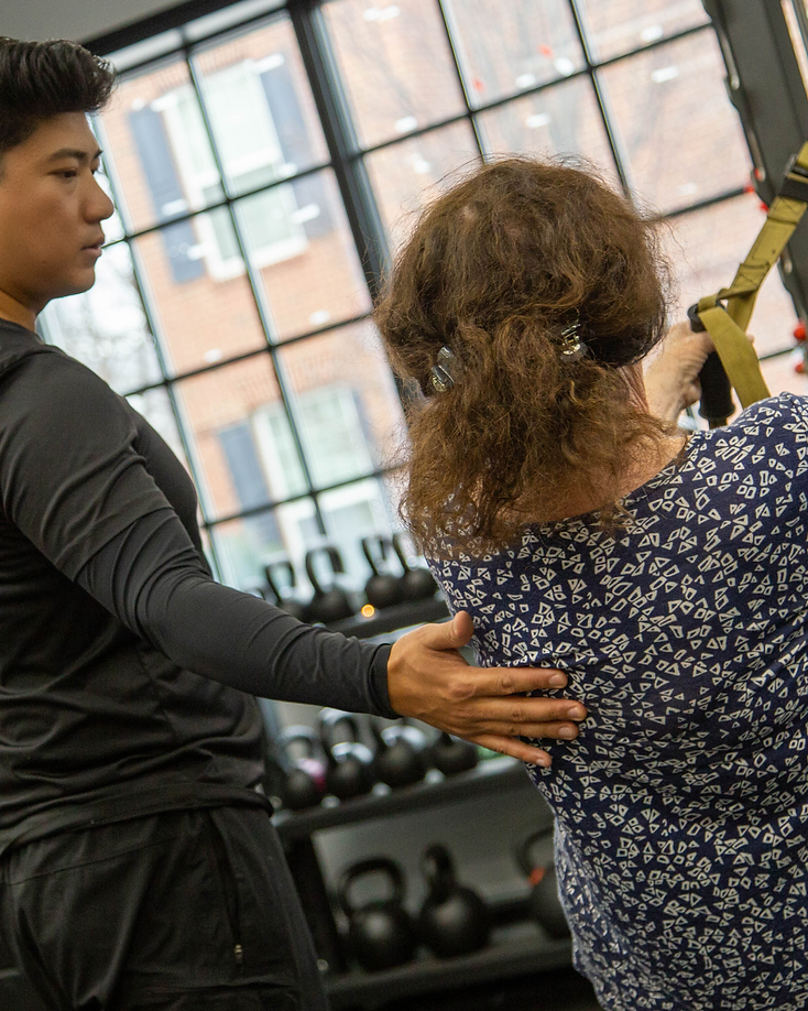 Migma Tamang providing hands-on guidance to a client during a suspension trainer exercise in the studio.