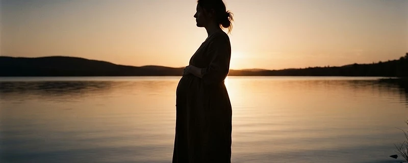 Pregnant woman silhouette at golden hour standing at the edge of still water