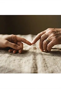 Two hands nearly touching over textured linen, warm window light