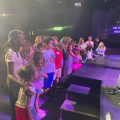 Children lined up on stage under purple and blue stage lights