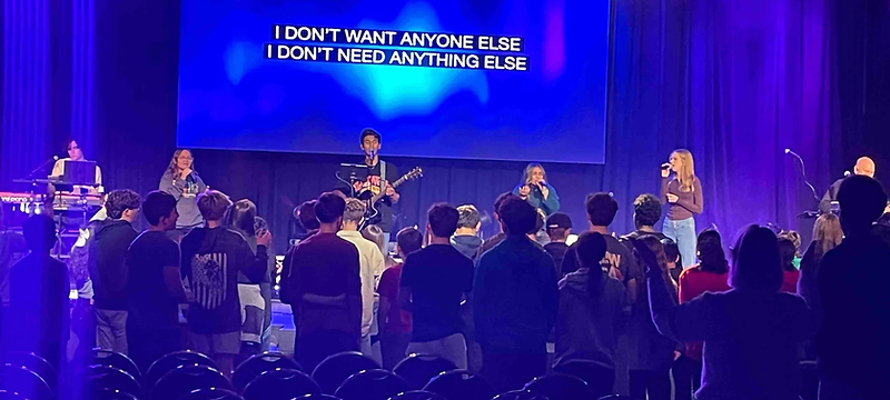 Worship band leading youth in praise with lyrics on screen