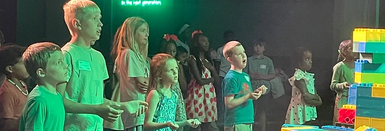 Children facing the stage under the greatness of the next generation sign