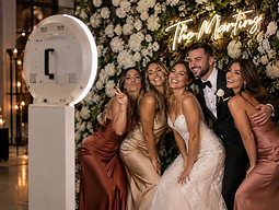 The wedding party posing in front of the Social Booth and floral wall