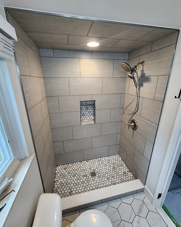 Walk-in shower with large-format grey wall tile, hex mosaic niche, and hex tile floor