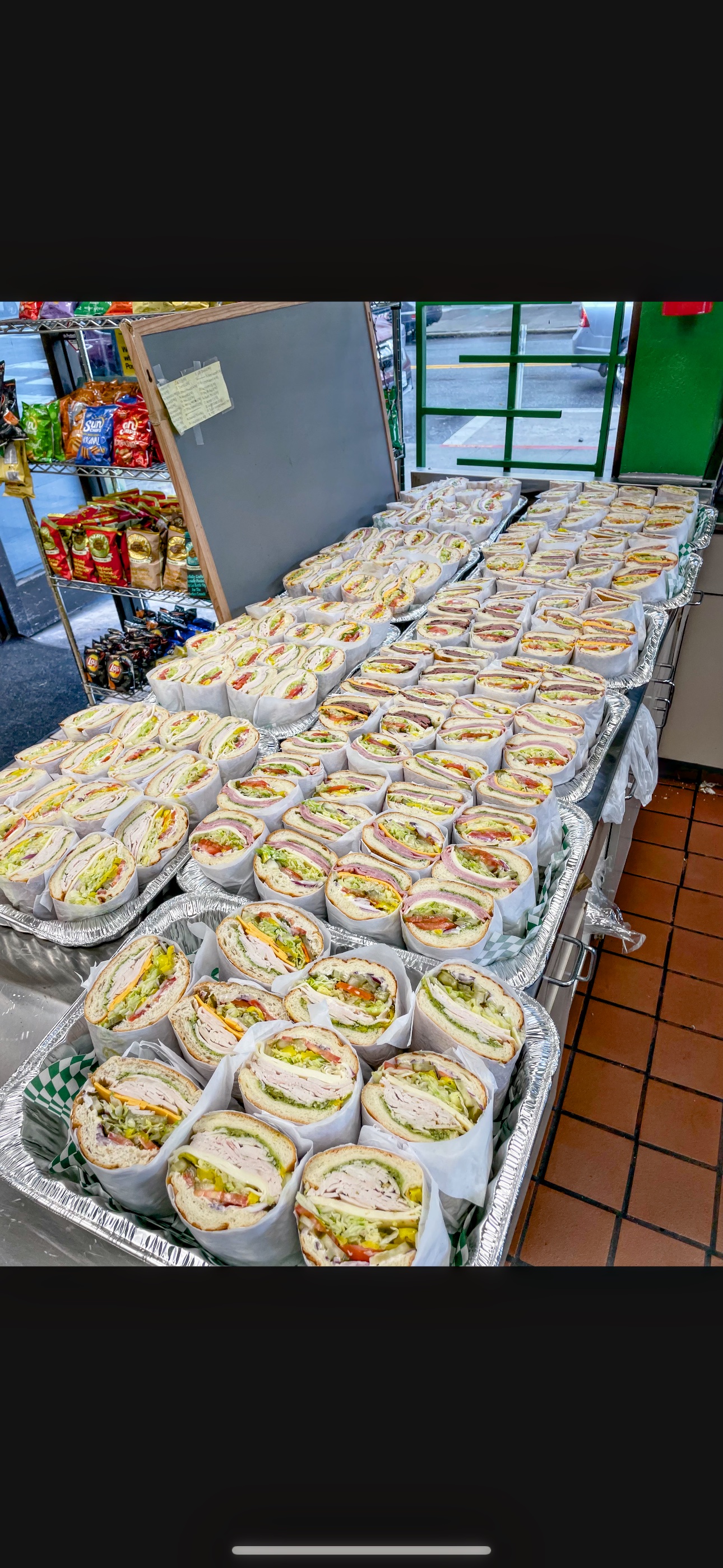 Trays of wrapped sandwich halves lined up on the deli counter for a catering order