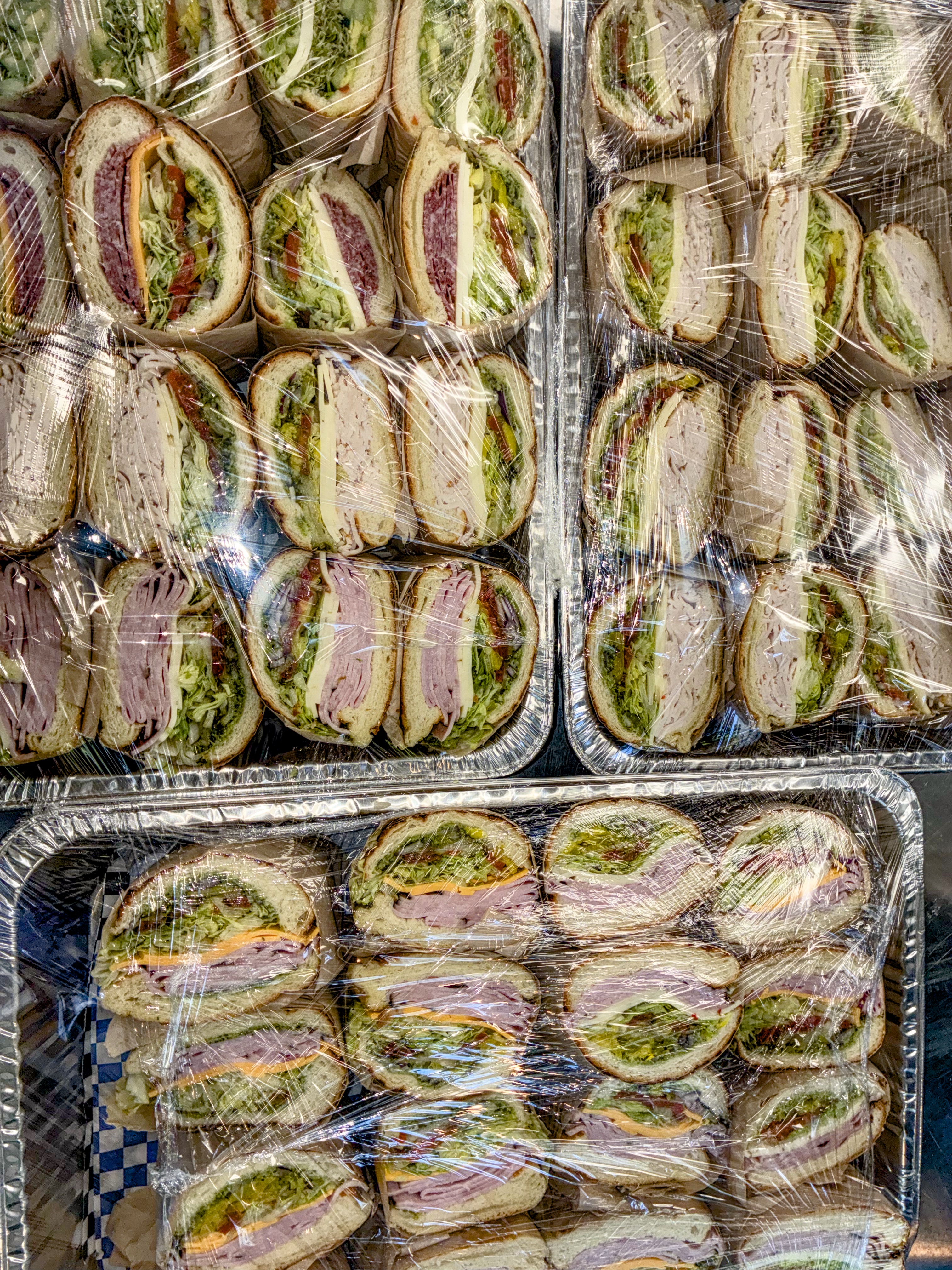 Foil trays of wrapped deli sandwiches ready for pickup