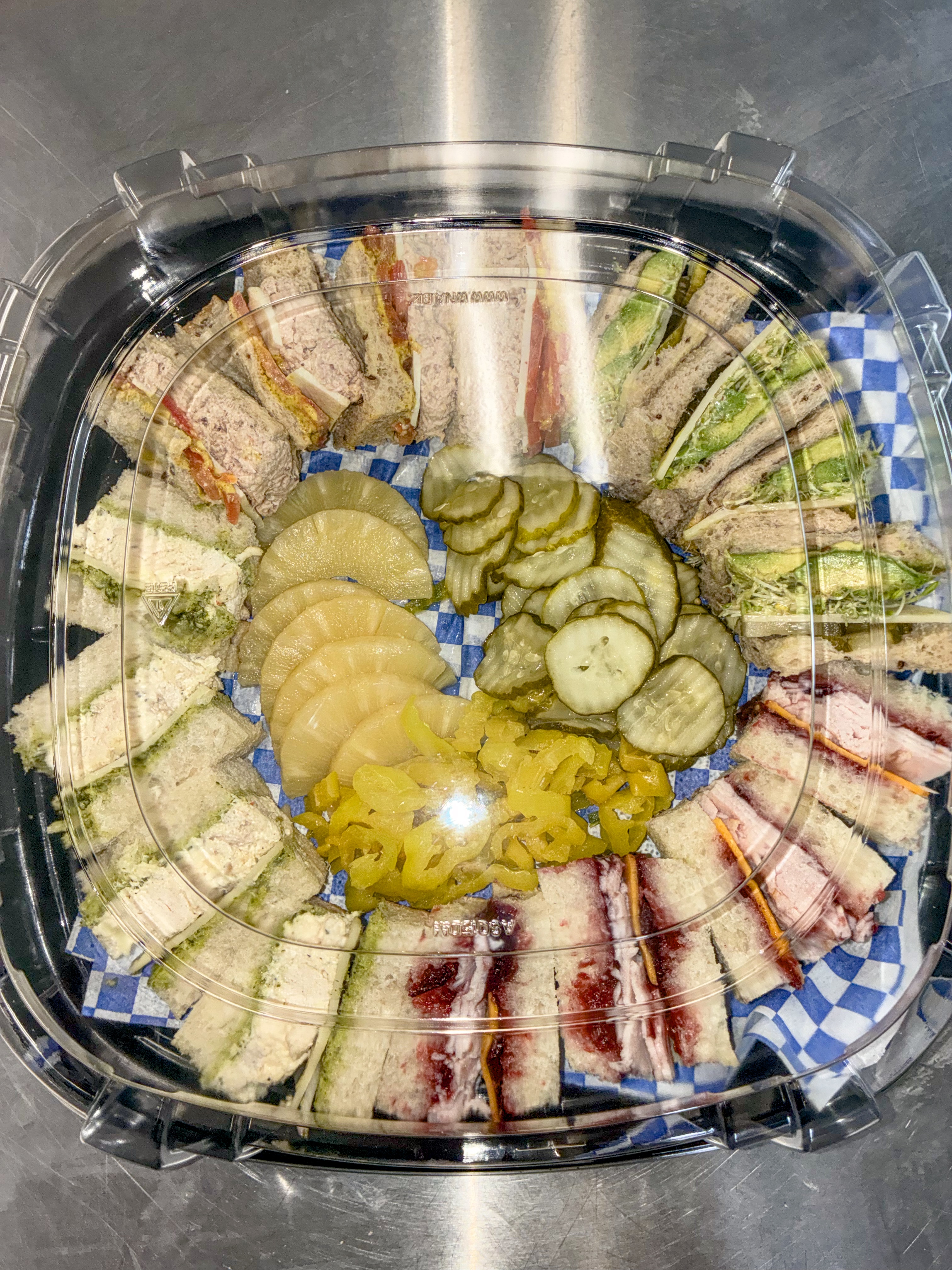 Party platter of quartered sandwiches arranged around pickles and pepperoncini