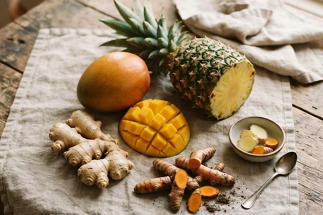 Fresh mango, pineapple, ginger and turmeric arranged on a linen-covered wooden table
